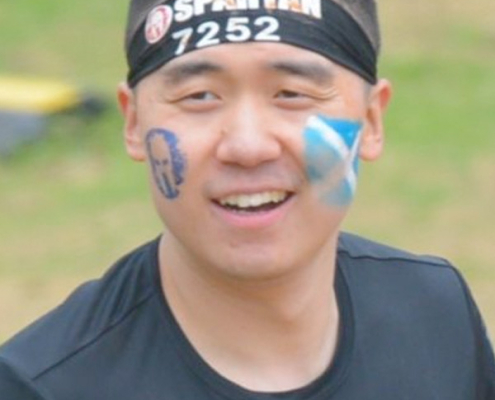 An image of Yuhao Sun, a young man of Asian heritage with very short black hair, taking part in a sporting event with a bandana reading "Spartan 7252" with a Spartan logo painted on one cheek, and a Saltire (Scottish flag) painted on the other cheek.
